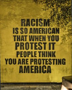 photo of a wall mural that states: Racism is so American that protest it and peple think you are prtesting America.