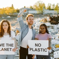 photo shows younger people with poster at a Plastic Dump Site, poster says No Plastic and Save The Planet