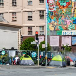Image of Homeless tents in San Francisco with Hotel behind them.
