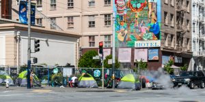 Image of Homeless tents in San Francisco with Hotel behind them.